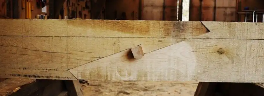 Close-up of wooden beam with angled scarf joint held by a wooden peg in a workshop.