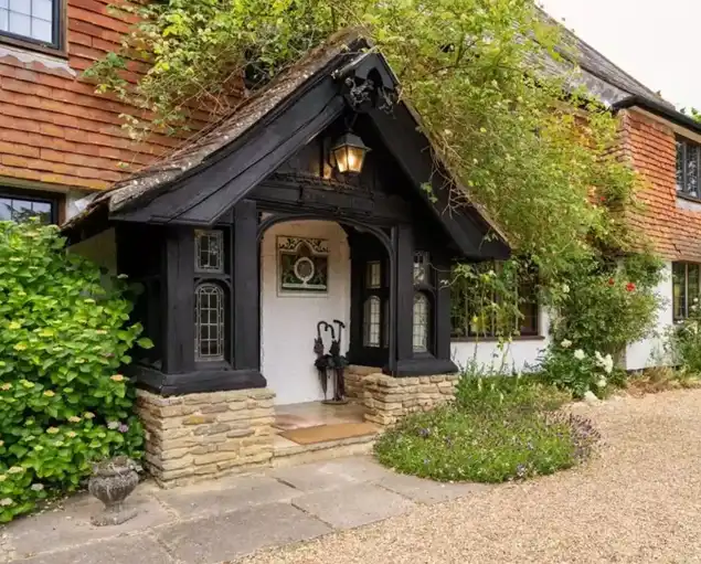 Cottage entrance with black timber frame, stone base, lantern light, and greenery around the doorway.